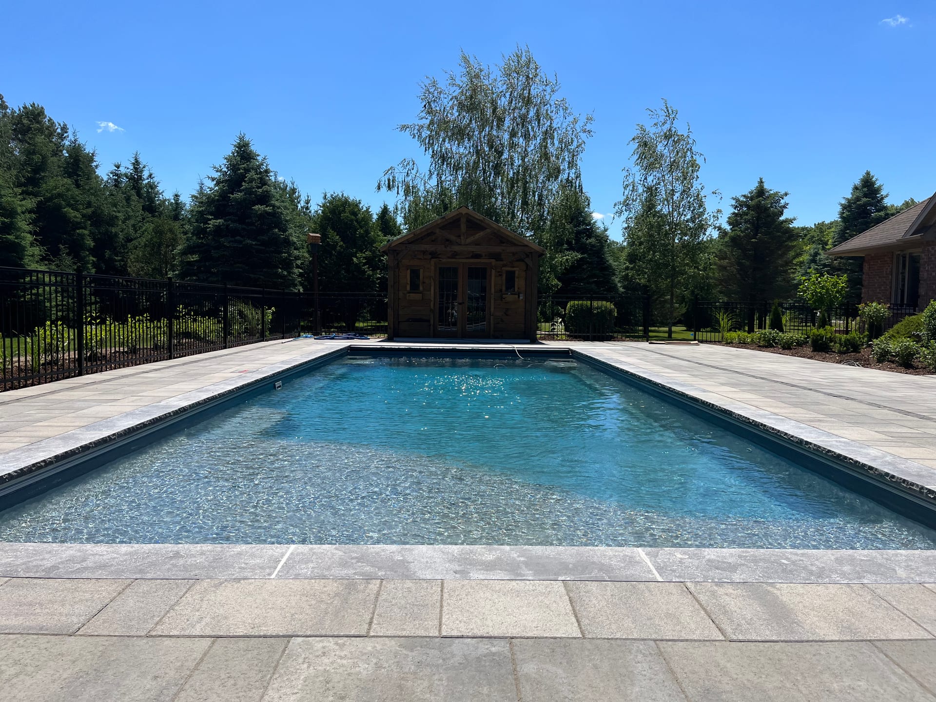 Fiberglass pool with cedar pool house and stone patio in London Ontario